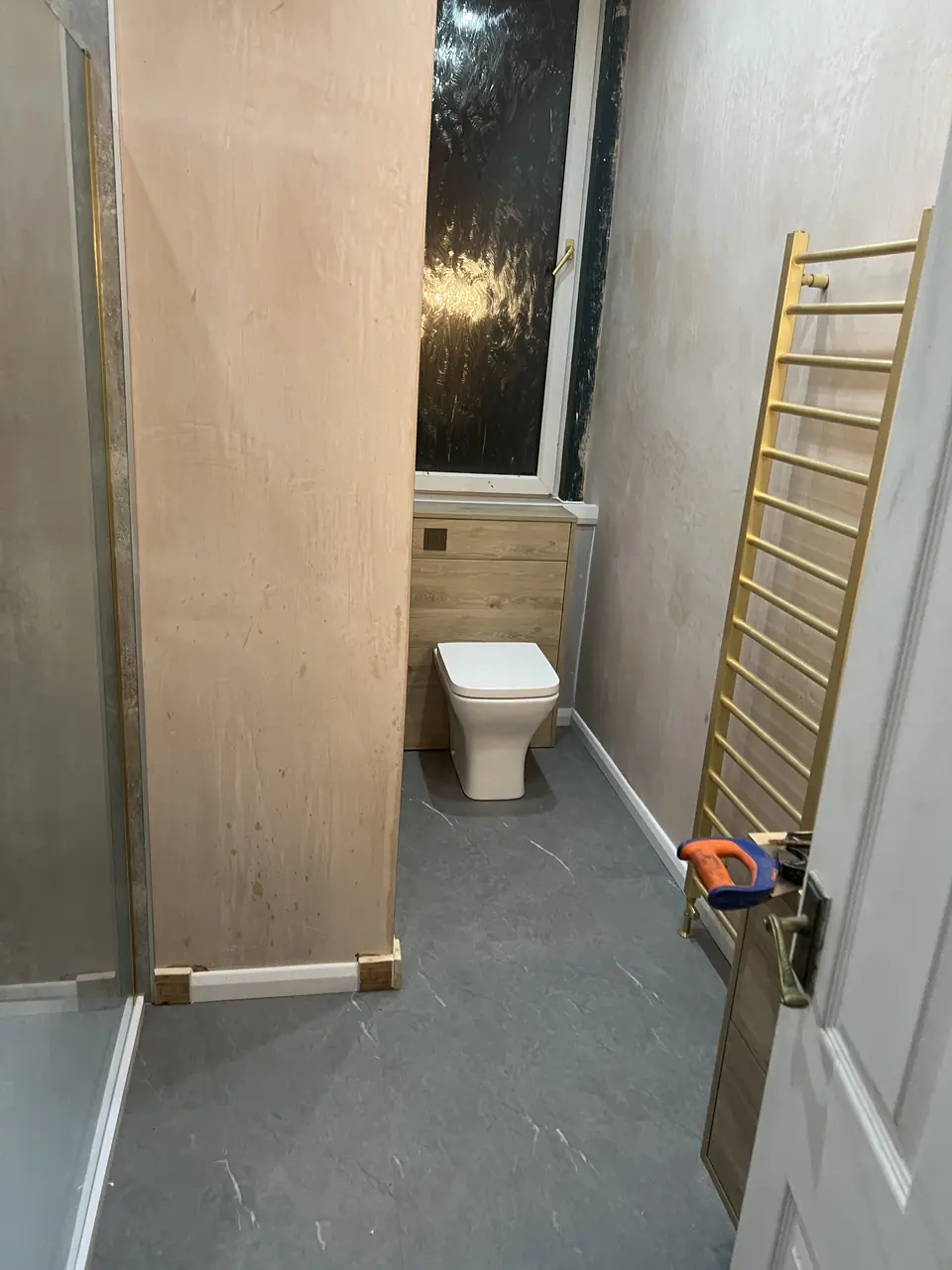 Bathroom mid-renovation with brass ladder towel rail and new toilet