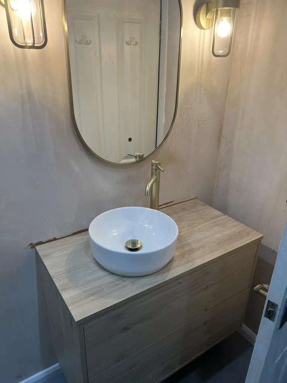 Brushed brass basin tap above a white vessel basin on a timber vanity
