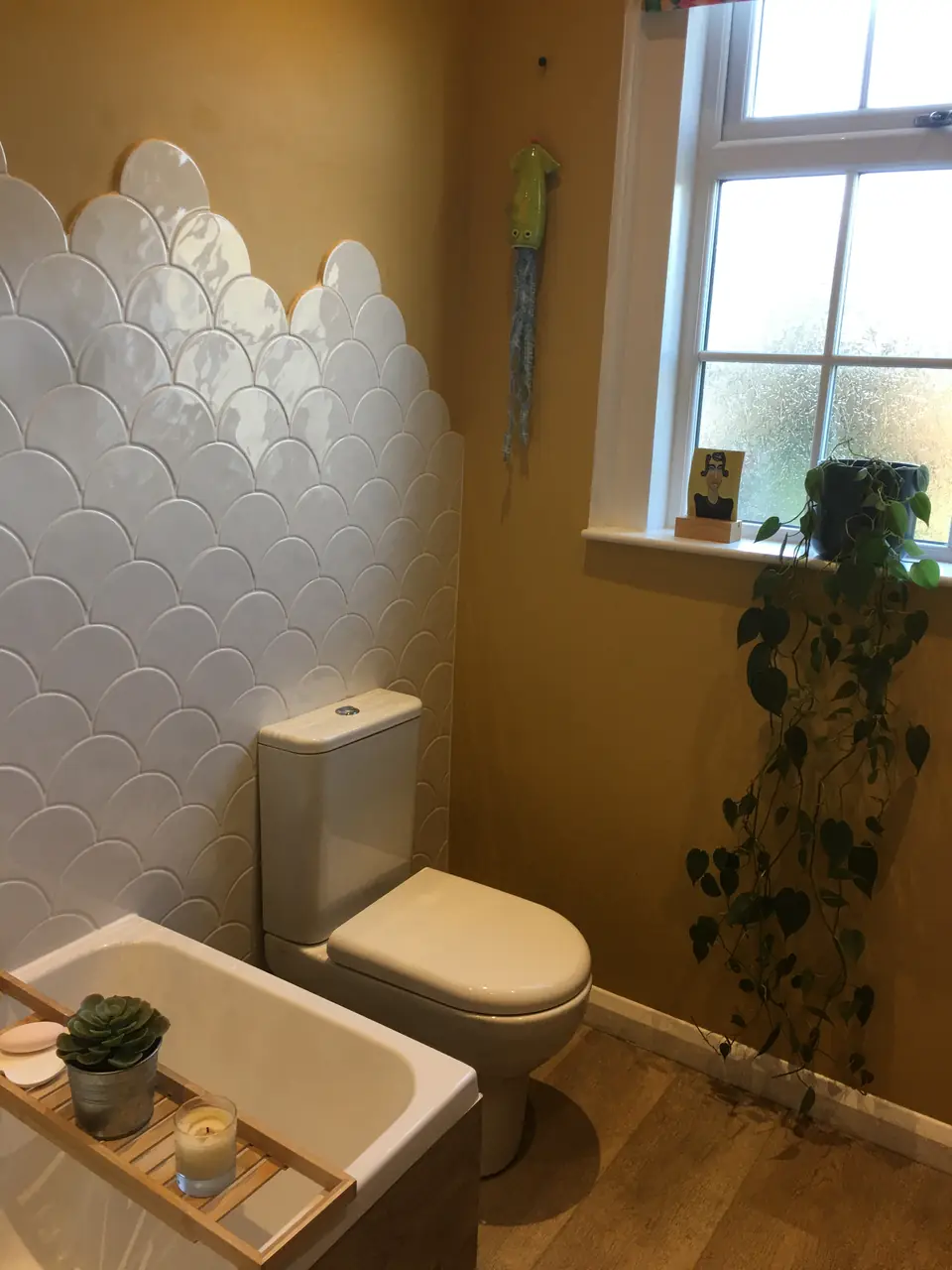 Renovated bathroom with white scallop wall tiles, bath with bamboo caddy and close-coupled toilet