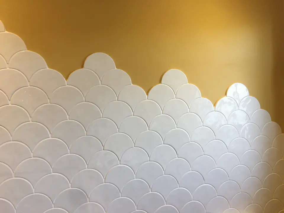 Close-up of white scallop tiles meeting a mustard painted wall