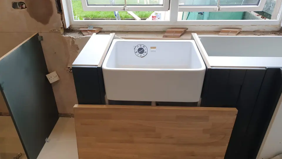 Belfast sink being fitted between dark green kitchen units