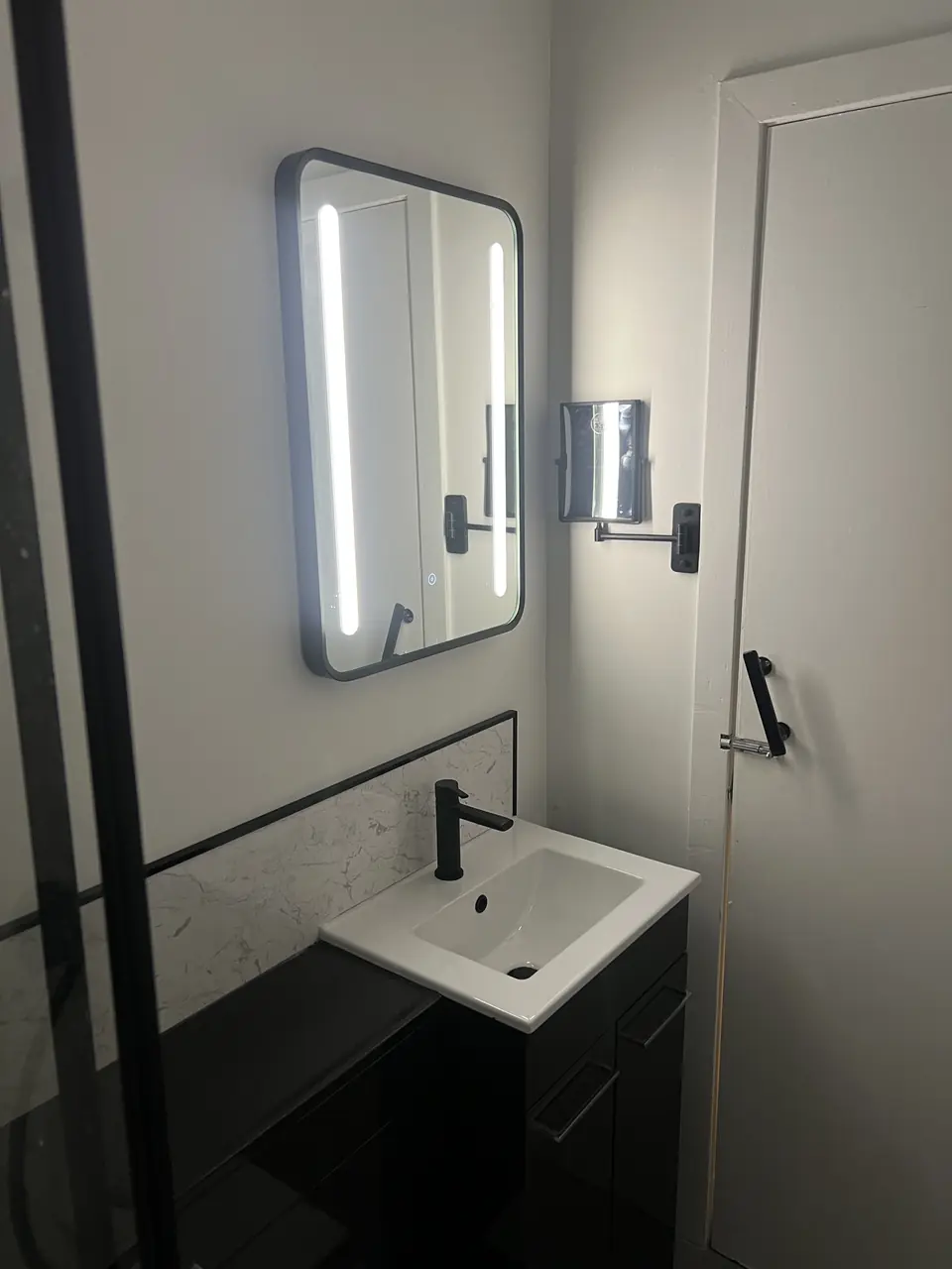Illuminated mirror above a white basin with black brassware