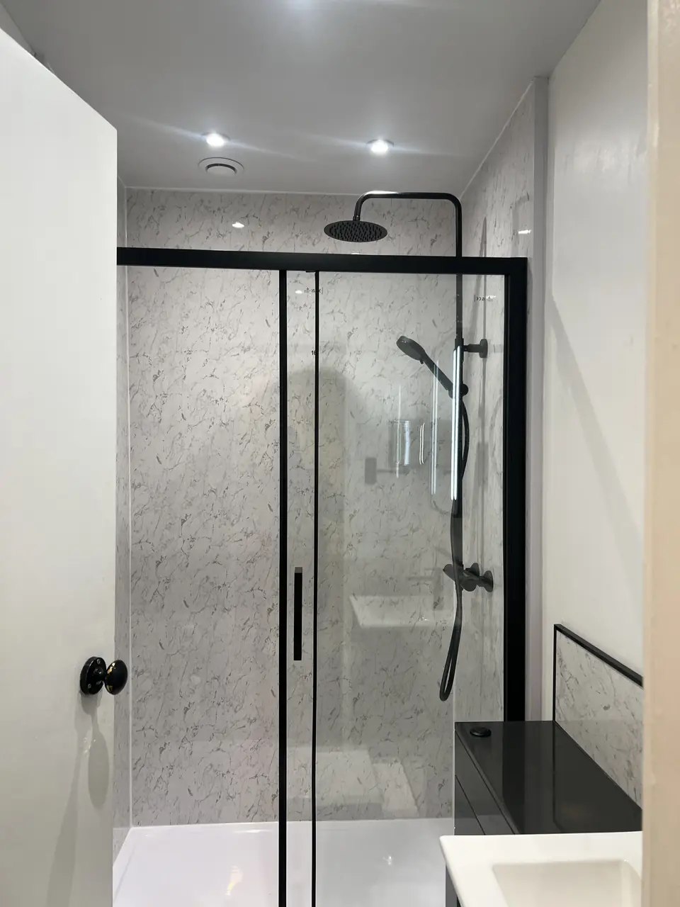 Walk-in shower with black-framed sliding doors and marble-effect panels